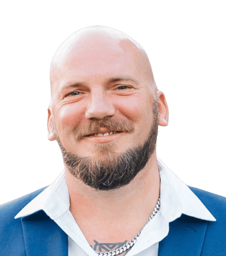Kevin Lunceford, a man with a neatly trimmed beard wearing a blue suit jacket, white shirt, and chain necklace, smiling at the camera against a plain background.