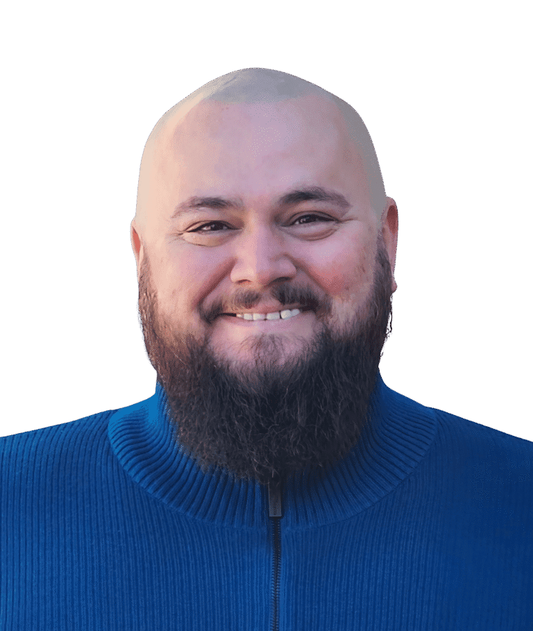 Shane Dewberry, a man with a full beard and mustache is smiling while wearing a blue zip-up sweater.