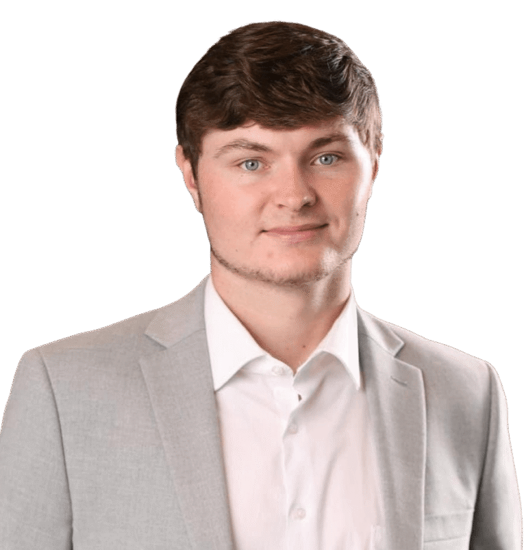 Carter Archer, a young man with short brown hair, is wearing a light gray suit jacket and a white shirt, posing against a plain white background.