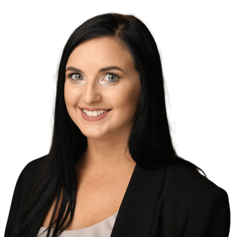 Haley Saliba, a woman with long black hair, wearing a black blazer and light top, smiles at the camera against a plain white background.