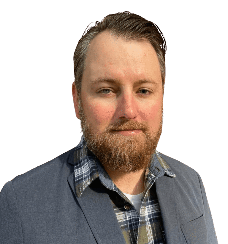 Jeremy Miller, a man with brown hair and a beard, is wearing a blue blazer over a plaid shirt as he stands against a plain white background.