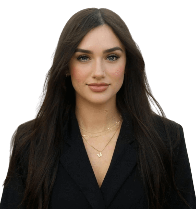 Makenzie Jones, a woman with long dark hair, wears a black blazer and layered gold necklaces as she poses confidently against a plain white background.