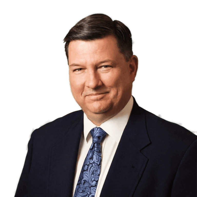 Rob Denning, a man in a dark suit, white shirt, and patterned blue tie poses against a plain white background.